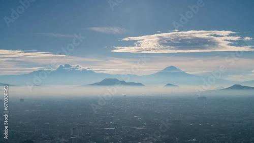 A high vantage point timelapse captures a breathtaking Mexico City valley sunrise, with the iconic active volcanoes Iztaccihuatl and Popocatepetl in the background. The smog and pollution are visible. photo