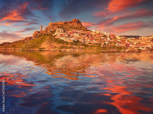 Old building of Castelsardo port reflected in the calm waters of Mediterranean sea. Majestic summer sunset on Sardinia island, Province of Sassari, Italy. Traveling concept background.