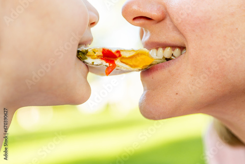 Woman and little girl sharing street food in the park. Mom and daughter eating together outdoors. Lifestyle, food, family concept