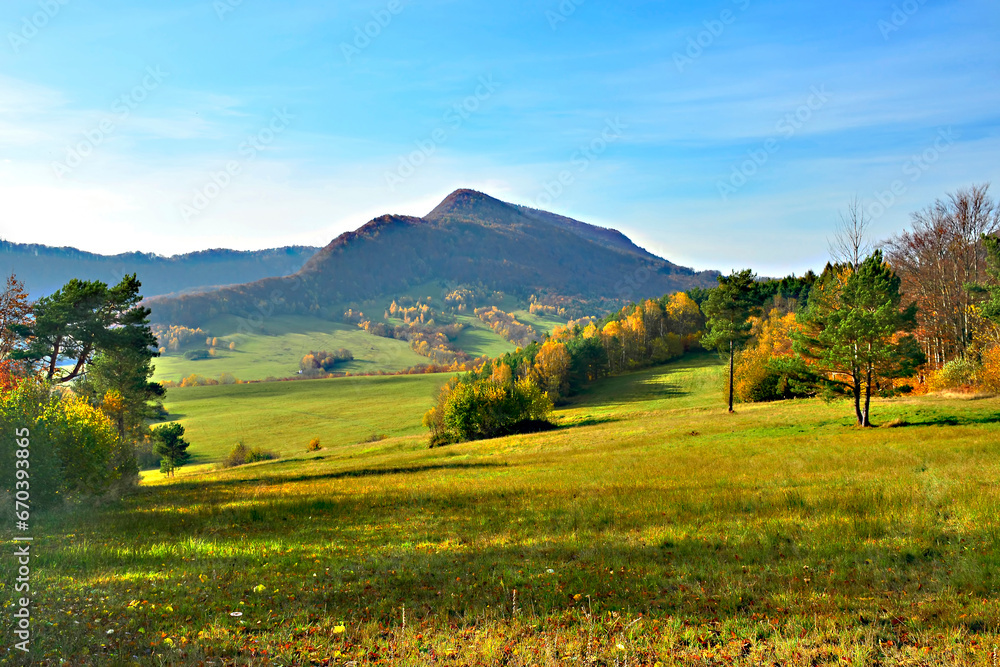 Autumn mountains landscape. Trees on a slope with dry grass and wooded mountains under blue sky with white clouds. View of Mountain Lackowa (997 msl) in Low Beskids. (Beskid Niski) - obrazy, fototapety, plakaty 