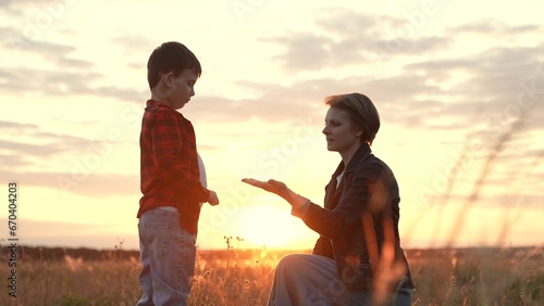 Boy gives hand to mother trusting on field at bright sunset of autumn evening