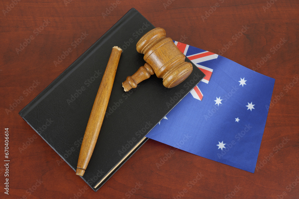 Broken gavel and legal book with flag of Australia on wooden table.