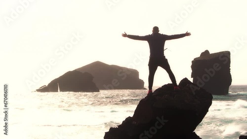 Silhouette of man standing at the beach over a rock with open arms. Vcations at the seashore concept photo