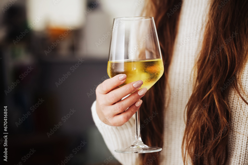 Woman drinking wine. White wine drinking. Wine glass in hand. Girl in woolen sweater. Cozy winter alcohol background. Female hand holding wine glass. Winter season clothing. Long hair shallow depth.