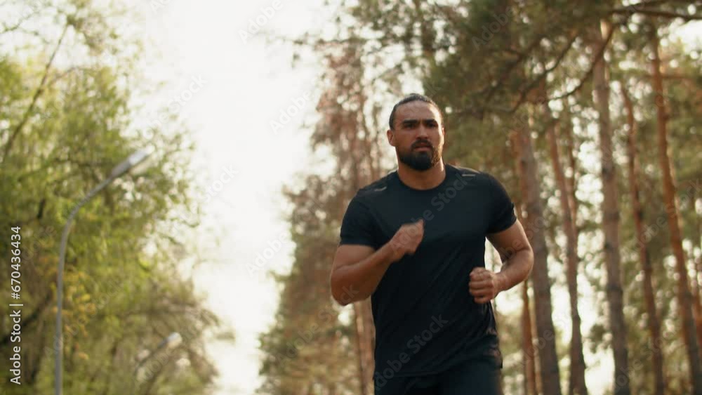 Young muscular athlete running at a leisurely pace with a tense face in a city park. Concept of modern outdoor sports training in a casual urban life Young muscular athlete running at a leisurely pace with a tense face in a city park. Concept of modern outdoor sports training in a casual urban life