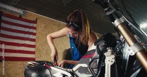 close-up shot: a girl auto mechanic repairs a motorcycle in her workshop with a screwdriver against the background of the US flag and tools in the garage photo