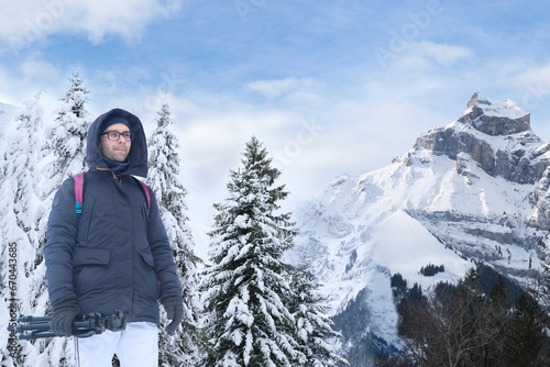 young pensive man in winter clothes, guy 30 years old against backdrop of snow-capped mountains in Switzerland, concept of popular tourist destinations, beauty snowy mountain peaks and natural wonders
