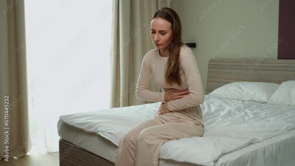 Young brunette suffers from abdominal pain while sitting on the bed. Young brunette suffers from abdominal pain while sitting on the bed.