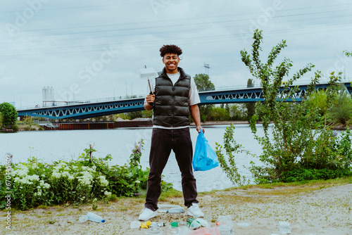 Portrait of smiling young man collecting garbage near river against sky photo