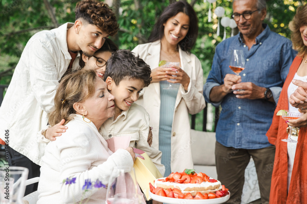 Senior woman embracing boy near family during dinner party Senior woman embracing boy near family during dinner party