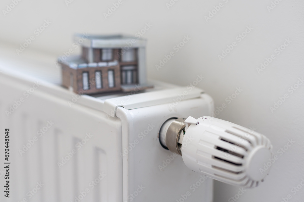 Close-up Of Heating Radiator With Model House In Front Of Blue Wall Close-up Of Heating Radiator With Model House In Front Of Blue Wall