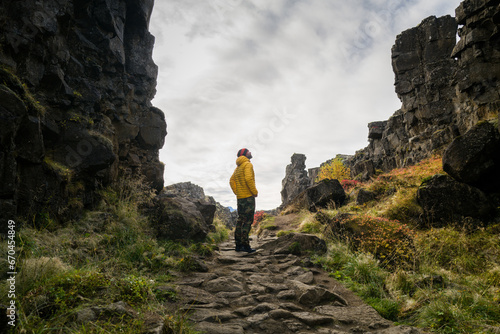 Man wearing a yellow jacket walking between the tectonic plates in the Thingvellir national park photo