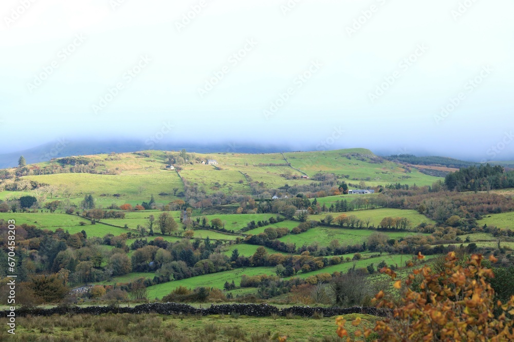 Landscape at Calry, County Sligo, Ireland in autumn featuring rolling hills of farmland fields bordered by stone walls and trees against backdrop of overcast skies