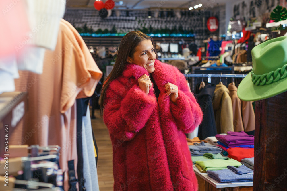 Young woman in fur coat choosing winter clothes in a clothing store.