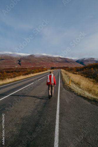Woman in a red jumper and a scarf walking on the road in Iceland