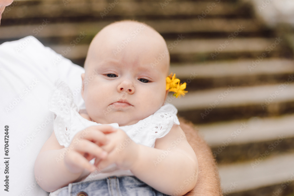 Portrait of newborn girl in white dress with yellow flower behind her ear, unrecognizable parent. Portrait of newborn girl in white dress with yellow flower behind her ear, unrecognizable parent.