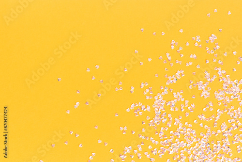 Silver crystal confetti scattered on a yellow background. Festive concept with copy space. © rorygezfresh