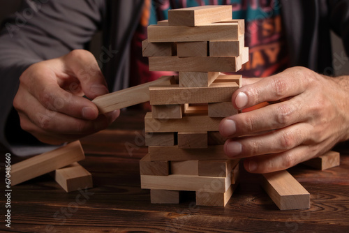 Hand of engineer playing a blocks wood tower game jenga on blueprint or architectural project