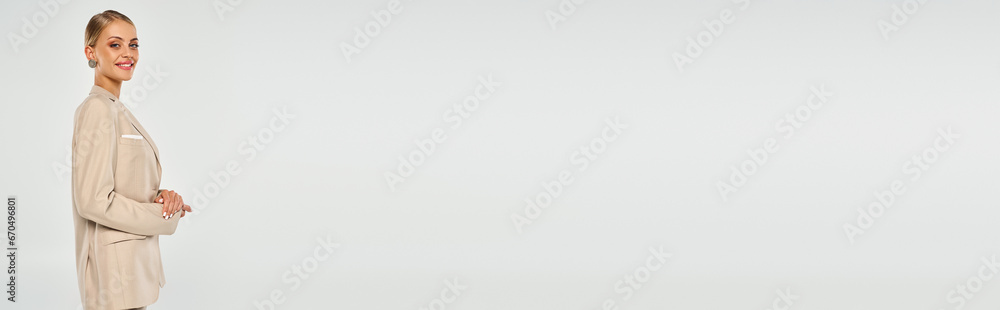 blonde woman in beige stylish suit smiling at camera on grey backdrop, fashion and beauty, banner blonde woman in beige stylish suit smiling at camera on grey backdrop, fashion and beauty, banner