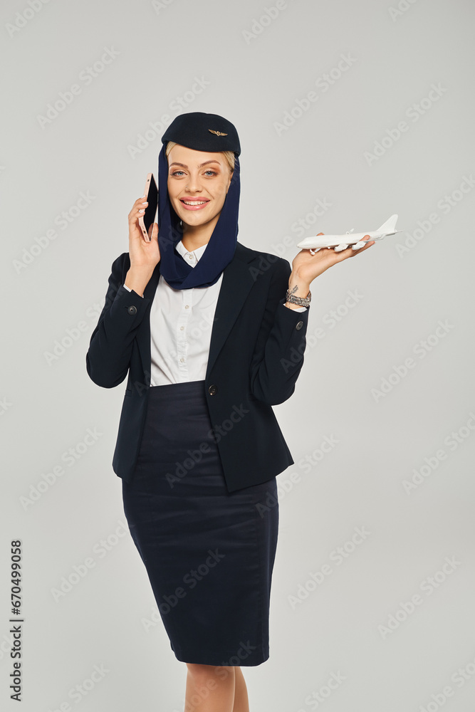 elegant arabian airlines stewardess with airplane model talking on smartphone on grey backdrop elegant arabian airlines stewardess with airplane model talking on smartphone on grey backdrop