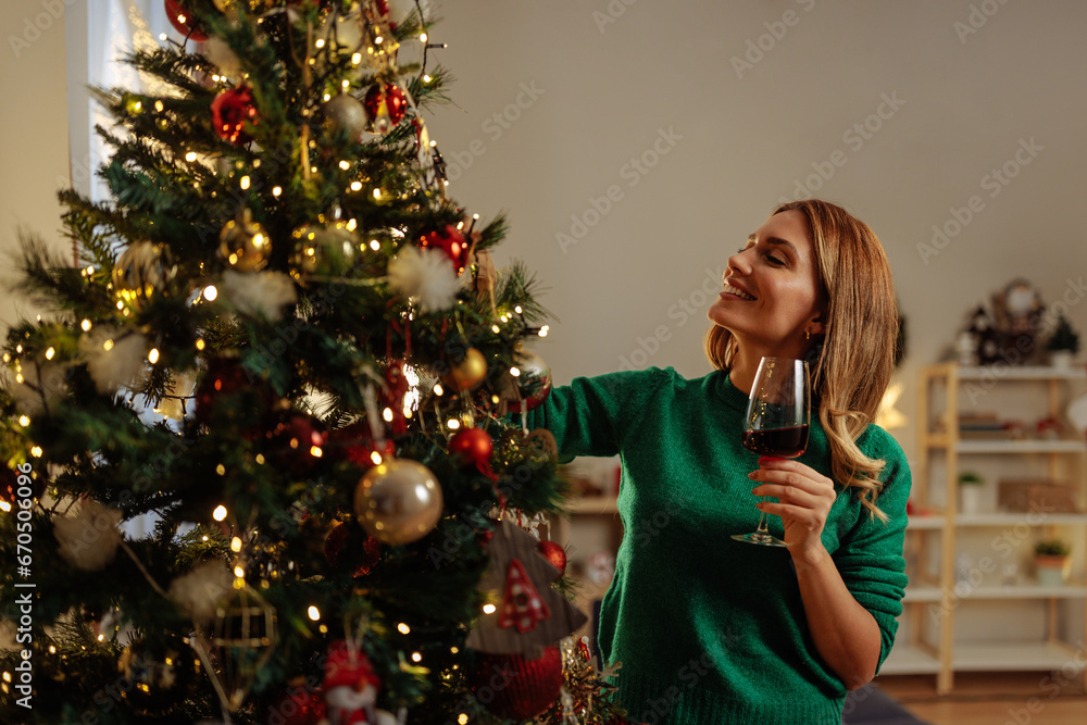 Woman decorating Christmas tree and drinking red wine Woman decorating Christmas tree and drinking red wine