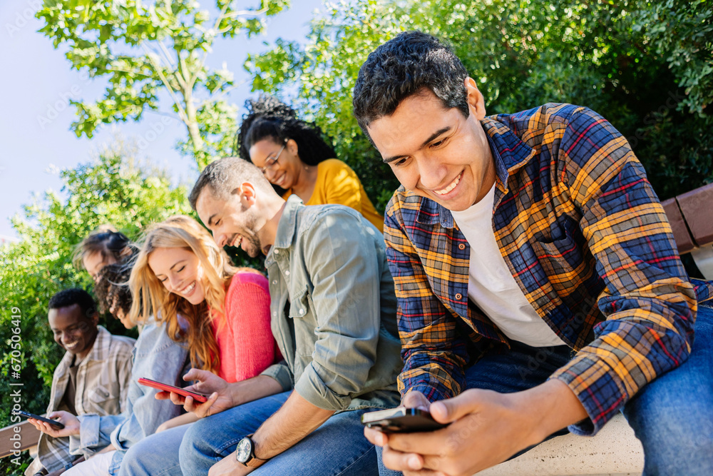 Young group of people using cell phones sitting together outside. Technology lifestyle concept with college student friends enjoying social media content on mobile phone network app. Young group of people using cell phones sitting together outside. Technology lifestyle concept with college student friends enjoying social media content on mobile phone network app.