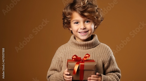 little cute boy holding gift box with ribbons on color background, child in knitted sweater, smiling happy kid, new year, christmas, eve, present, kindergarten, childhood, holiday, winter, toddler © Julia Zarubina