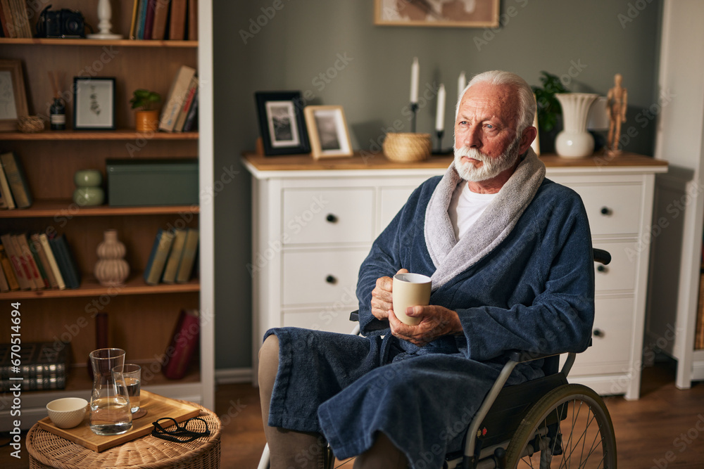 Elderly man sitting in wheelchair drinking coffee in the living room Elderly man sitting in wheelchair drinking coffee in the living room