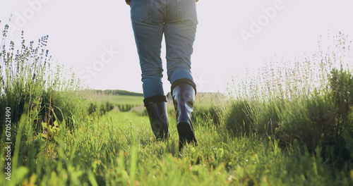 Farmer in rubber boots outdoors in field. Working agronomist walk on black earth soil. Legs of woman farmer in boots walking along agricultural field with sprouts at sunset with sun. Small family