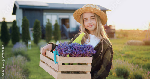 Fotografie Portrait of little girl garnered wearing hat looking at the camera holding a box of flowers