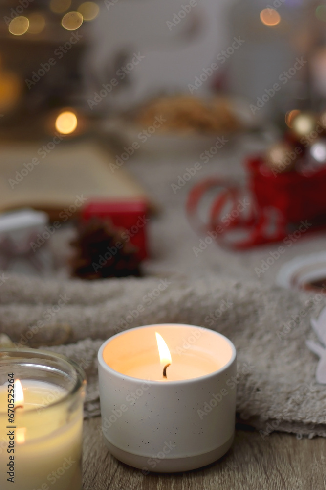 Bowl of cookies, cup of tea, dry oranges, pine cones, books, reading glasses, small presents, various Christmas decorations and lit candles on the table. Cozy Christmas hygge. Selective focus.