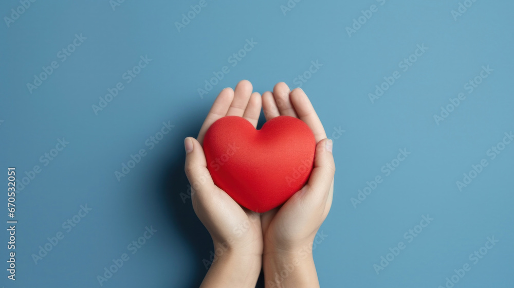 Fototapeta premium Hands holding a red heart on a blue background.