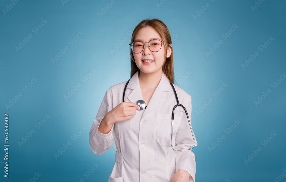 Portrait of smiling female doctor using stethoscope to listening heartbeat and looks at the camera. Young asian doctor wear medical uniform lab coat and stethoscope isolated over blue color background Portrait of smiling female doctor using stethoscope to listening heartbeat and looks at the camera. Young asian doctor wear medical uniform lab coat and stethoscope isolated over blue color background