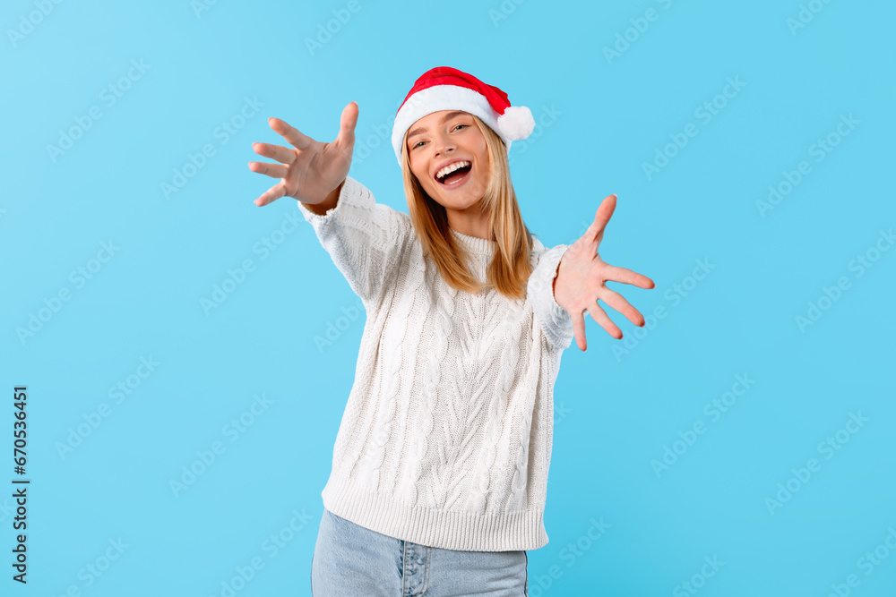 Excited woman in Santa hat reaching out at camera on blue backdrop