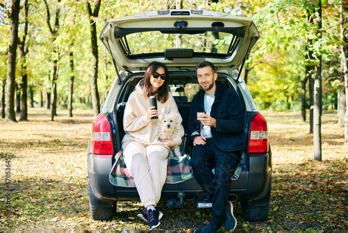 Couple with their dog relaxing in forest sitting in car trunk