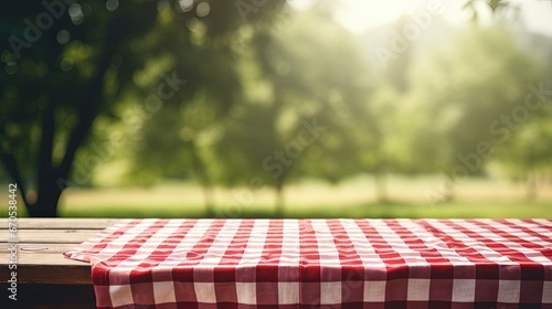Red checkered picnic cloth on wooden table empty space blurred nature background.