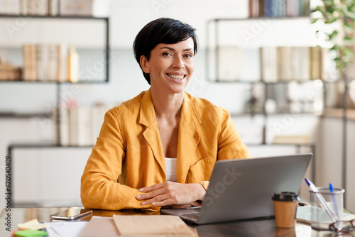 Middle aged business woman at desk posing with laptop indoor photo