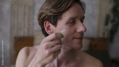 Young man doing facial massage using gua sha scraper. The concept of male cosmetology and care for you and your face photo