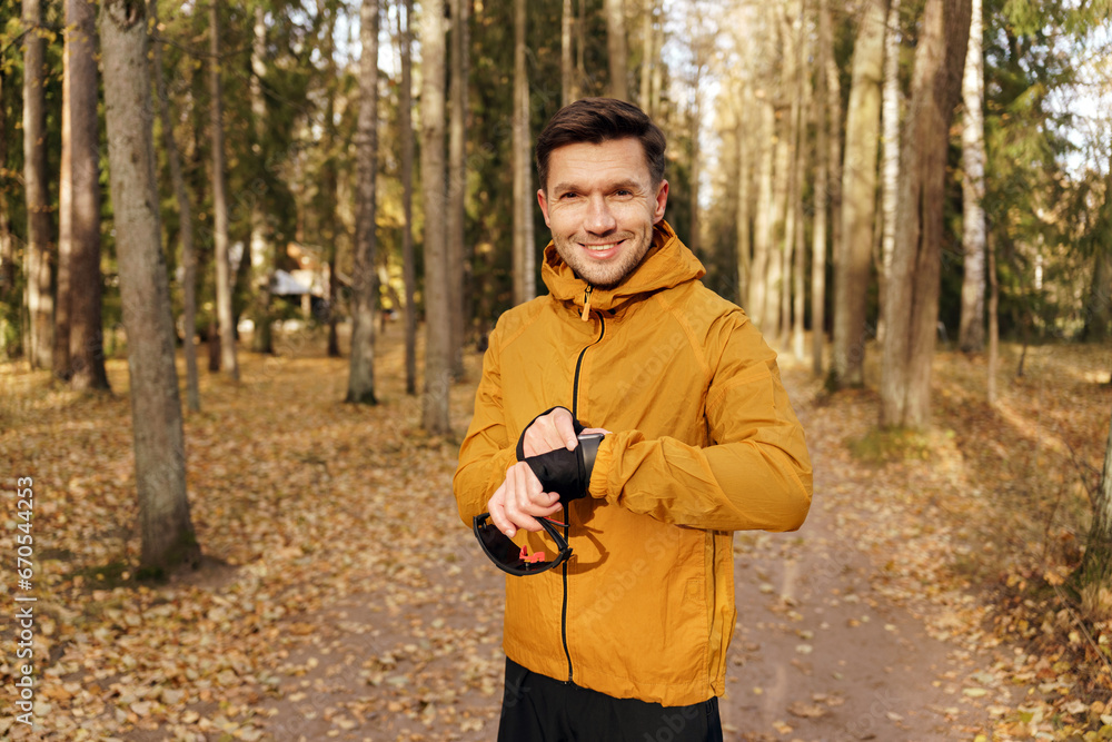 Looks at the camera uses a fitness app and watch, a runner trainer does an exercise. The athlete is active and healthy in winter in the park. A confident and hardy man. Looks at the camera uses a fitness app and watch, a runner trainer does an exercise. The athlete is active and healthy in winter in the park. A confident and hardy man.