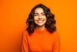 Jeune femme souriante posant avec un pull orange sur fond orange