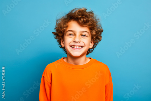 Portrait studio d'un jeune garçon souriant portant un pull orange sur fond bleu photo