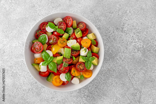 Caprese salad with cherry tomatoes, mini mozzarella balls, avocado, pesto sauce and fresh basil. Healthy vegetarian meal.