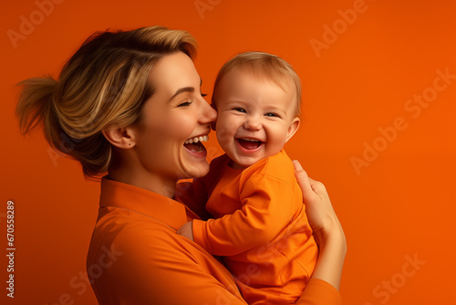 Le portrait d'une femme heuseuse et souriante tenant son enfant dans les bras, sur un fond isolé de couleur orange. photo