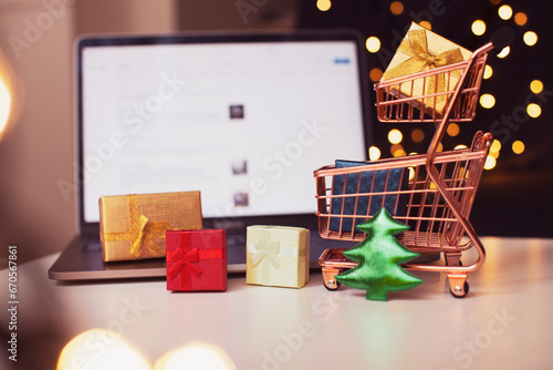 Shopping cart, gift boxes, laptop, Christmas tree on the blurred background with bokeh. Christmas shopping online.