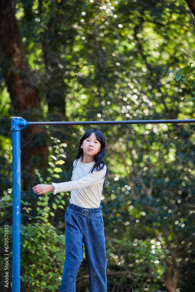 Fototapeta premium 秋の公園で鉄棒を遊んでいる小学生の女の子の様子