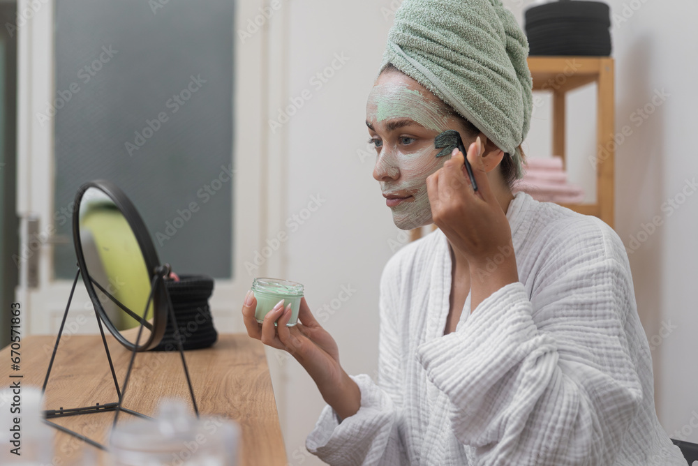 Organic Elegance: A woman, in her bathrobe, enhances her skincare with a clay mask applied using a brush, savoring the reflection in the mirror. Organic Elegance: A woman, in her bathrobe, enhances her skincare with a clay mask applied using a brush, savoring the reflection in the mirror.