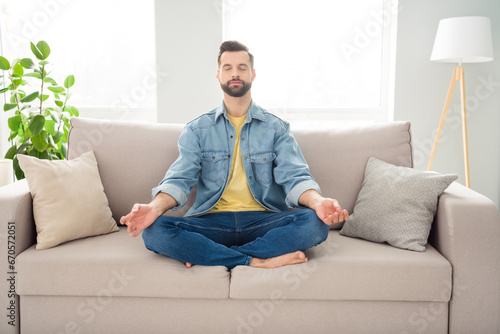 Full length body size young millennial in jeans outfit meditating sitting on couch at home