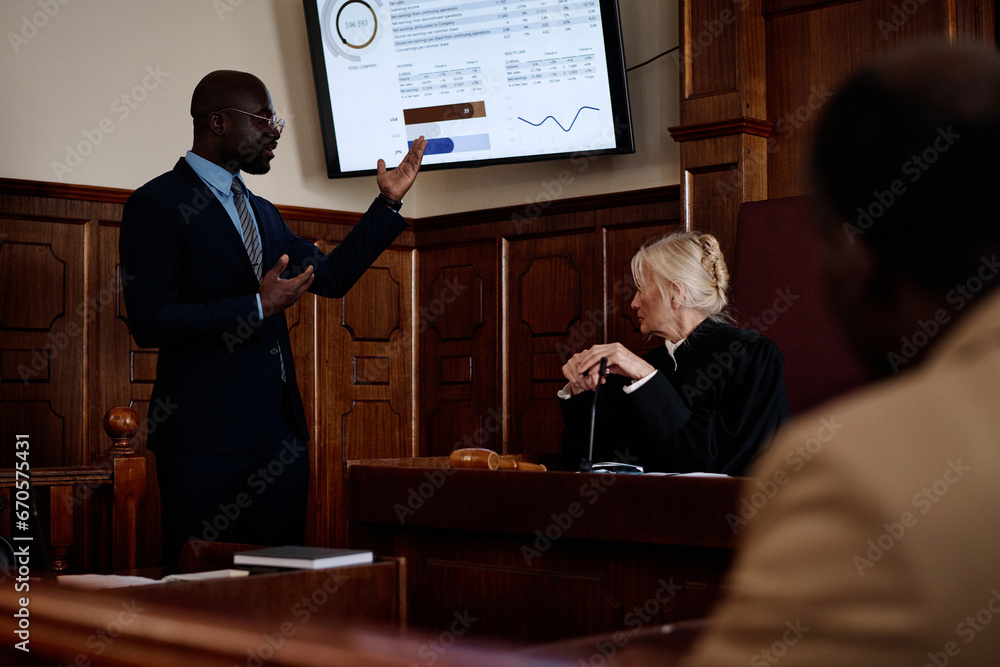 Confident African American lawyer in formalwear pointing at screen with summary of results while explaining data to mature female judge - obrazy, fototapety, plakaty 