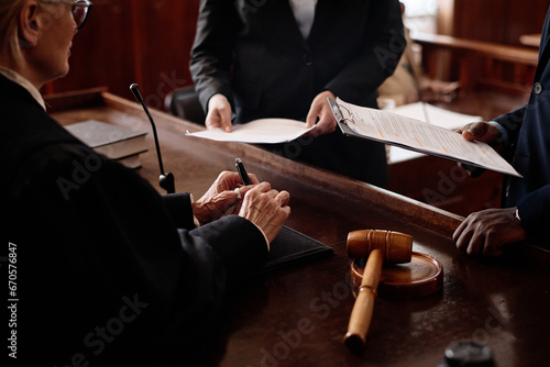 Close-up of accusation and protection sides with juridical documents standing in front of female judge during discussion of case points