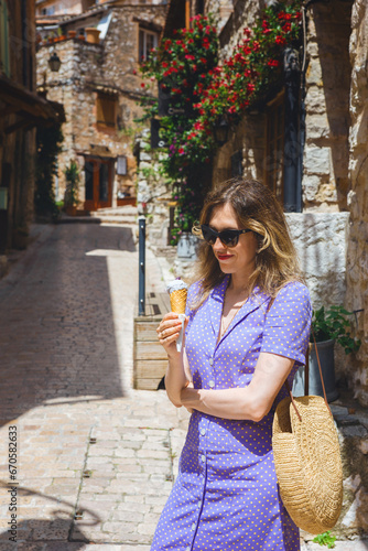 A young woman with violet ice cream in her hand walks along the ancient streets of the medieval town of Tourettes-sur-Loup, France